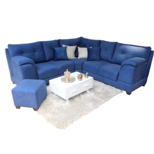 Juego de Sala L Italiana Gold con sofá en forma de L y puff, tapizado en tela azul sobre alfombra blanca.